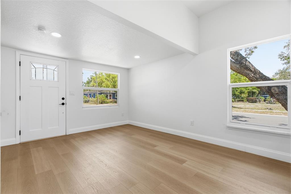 An empty room with white walls, light wood flooring, a front door, and two windows — 1700 SCRANTON STREET S, ST PETERSBURG, FL