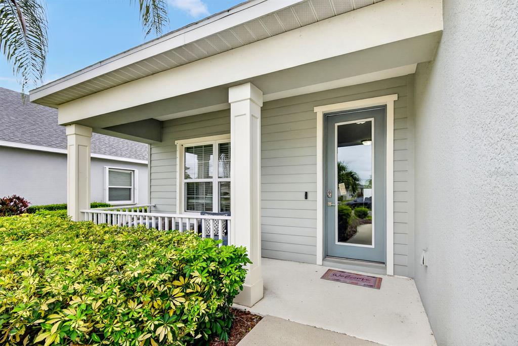 A covered front porch features light gray siding, a glass-paneled door, and a white railing — 7428 RIDGELAKE CIRCLE, BRADENTON, FL