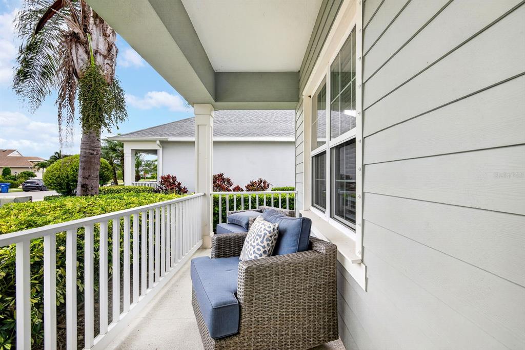A covered porch features wicker armchairs with blue cushions and white railings overlooking a yard — 7428 RIDGELAKE CIRCLE, BRADENTON, FL