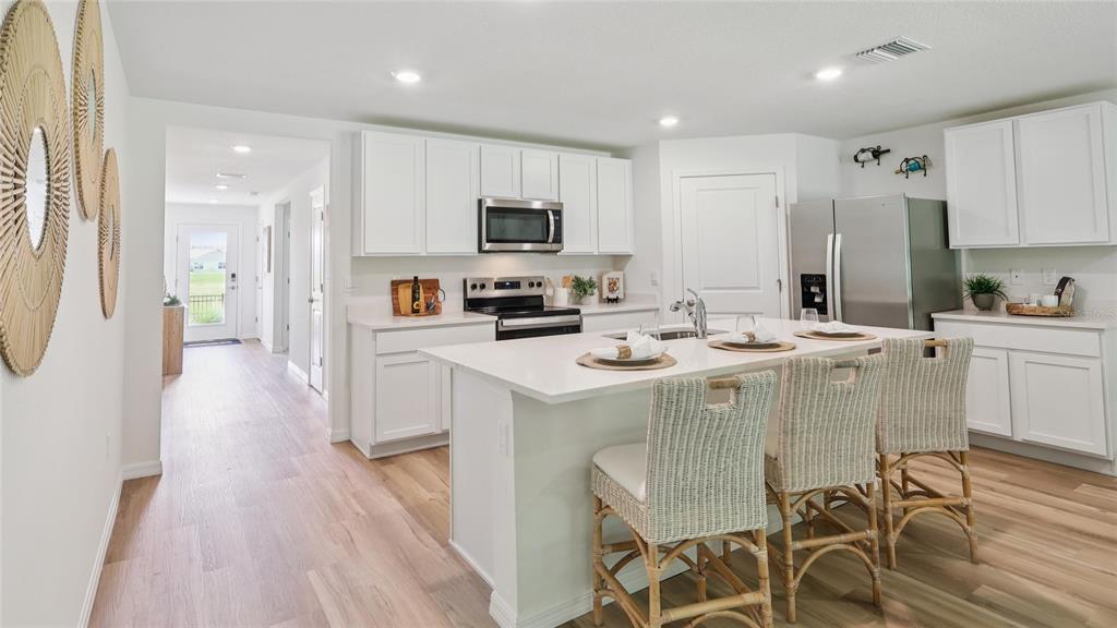 A modern kitchen features white cabinetry, a central island with bar stools, and stainless appliances — 17271 SW 39TH CIRCLE, OCALA, FL