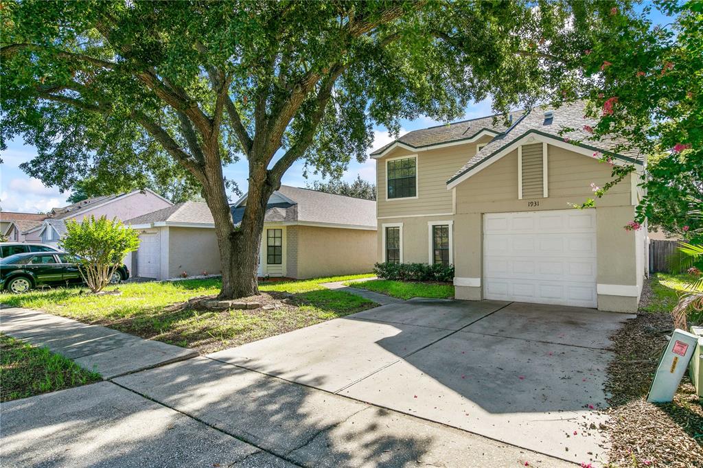 A two-story house with a beige exterior, a white garage door, and a large tree — 1931 SHEELER OAKS DRIVE, APOPKA, FL