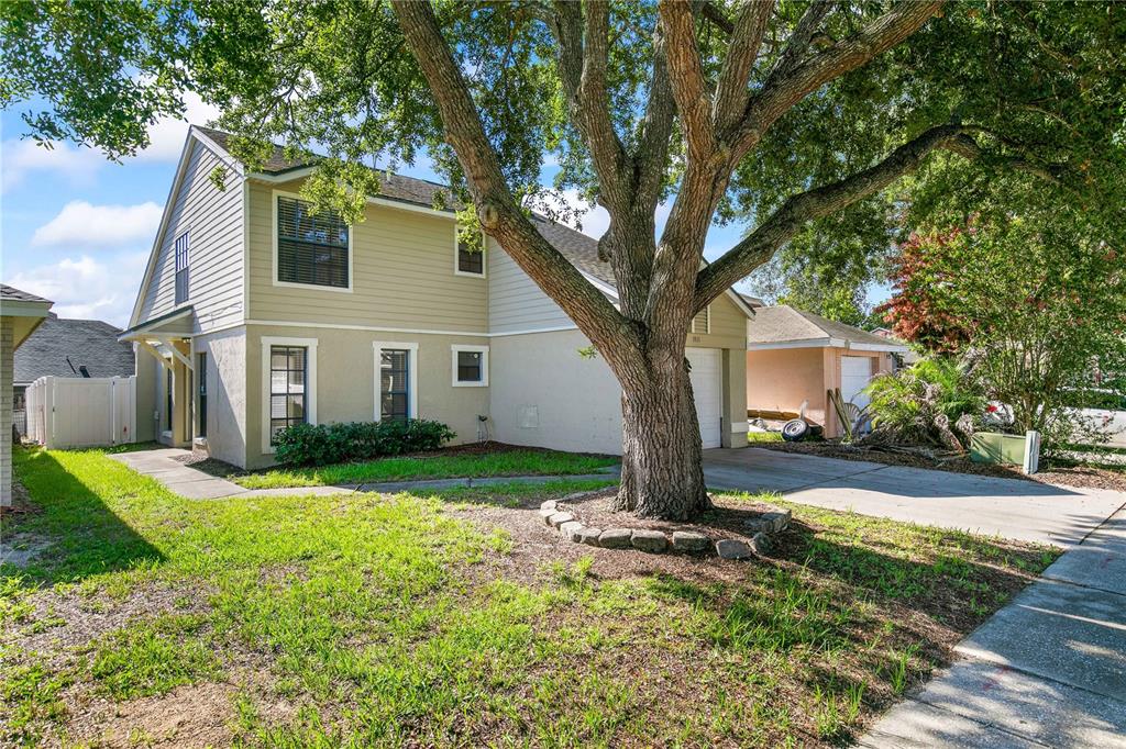 A two-story house with beige siding and stucco features a large tree in the front yard — 1931 SHEELER OAKS DRIVE, APOPKA, FL