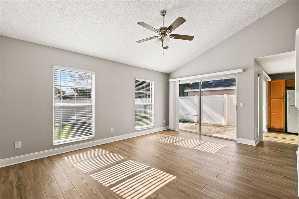 A living room with wood-look tile flooring, a vaulted ceiling, ceiling fan, and sliding doors — 1931 SHEELER OAKS DRIVE, APOPKA, FL