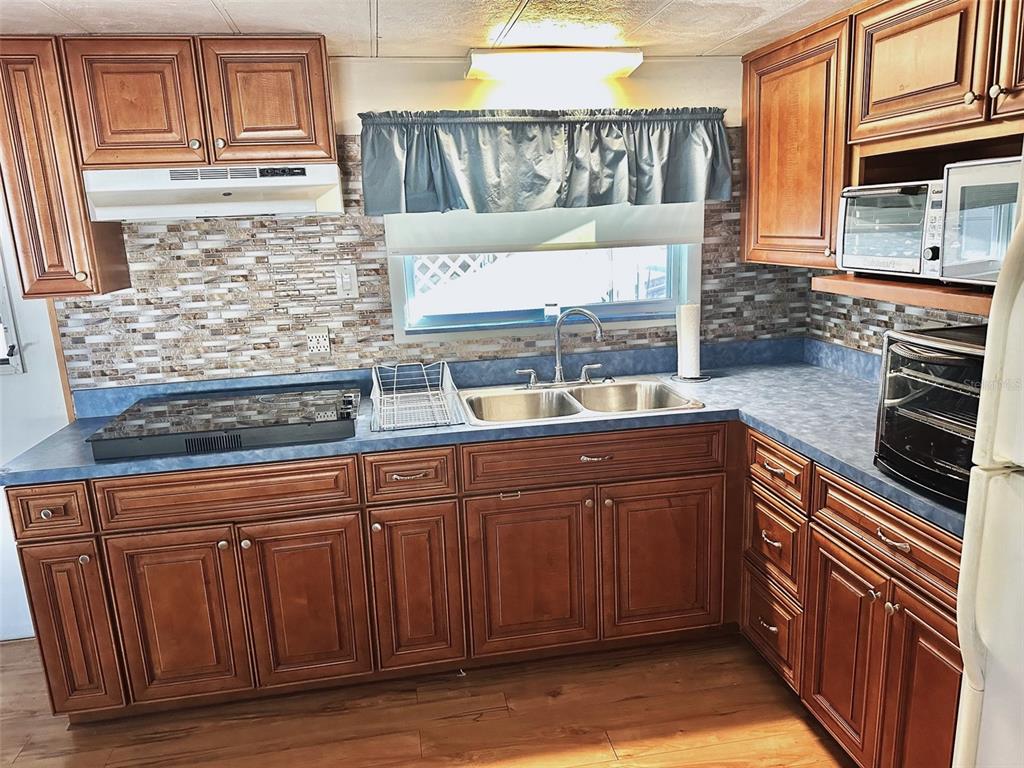 A kitchen features wood cabinets, a blue countertop, a mosaic backsplash, and a double sink — 9790 66TH STREET N UNIT 330, PINELLAS PARK, FL