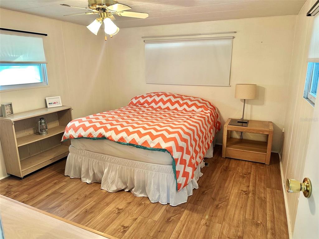 A bedroom features a bed with an orange chevron quilt, wood flooring, and a ceiling fan — 9790 66TH STREET N UNIT 330, PINELLAS PARK, FL