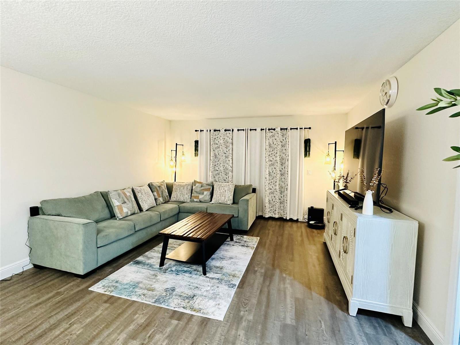 A living room features a green sectional sofa, a wooden coffee table, and a media console — 2200 S Cypress Bend Drive # 802, Pompano Beach FL 33069, POMPANO BEACH, FL