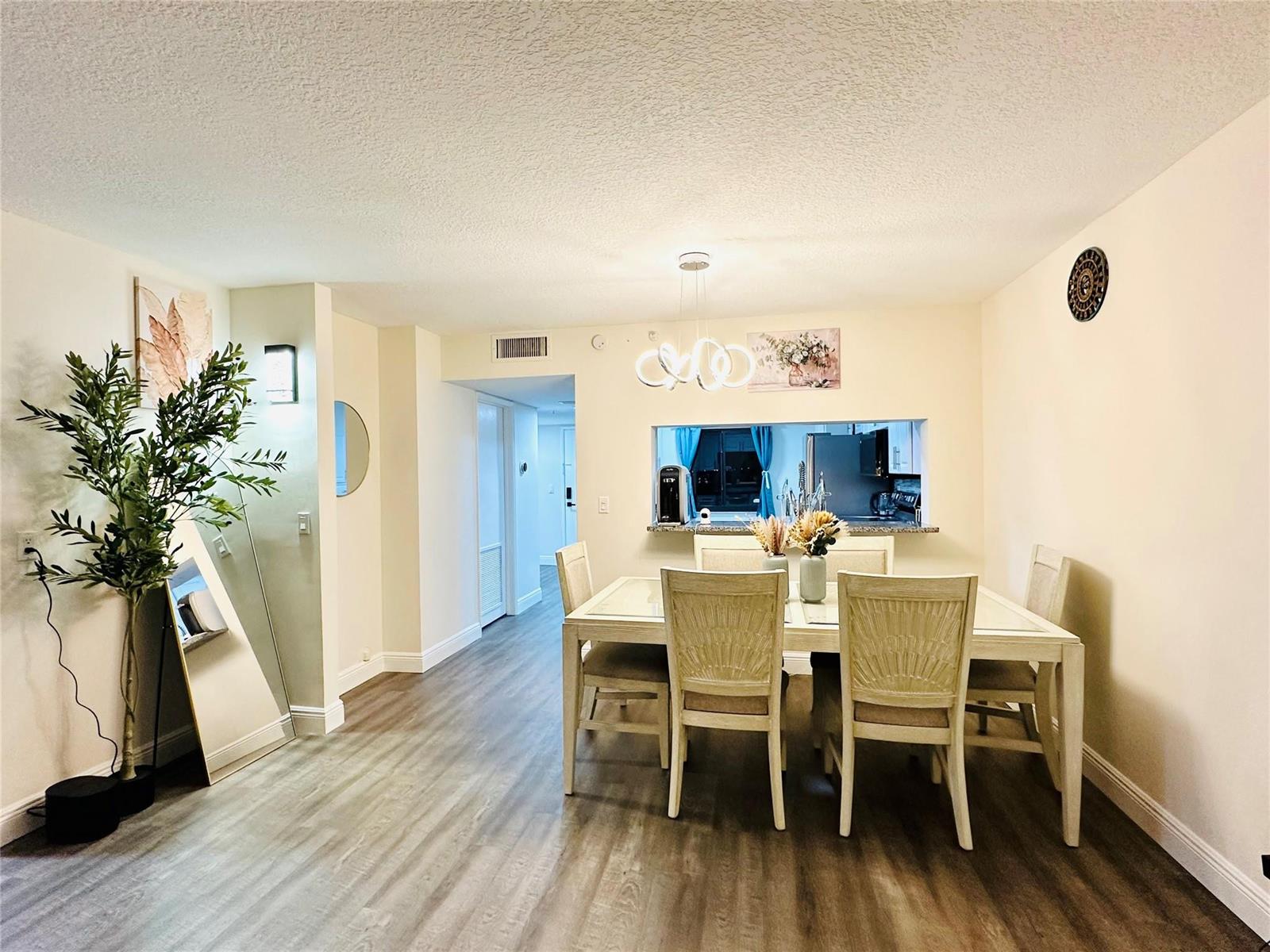 A dining area features a light-colored table with four chairs, wood-look flooring, and a pass-through — 2200 S Cypress Bend Drive # 802, Pompano Beach FL 33069, POMPANO BEACH, FL