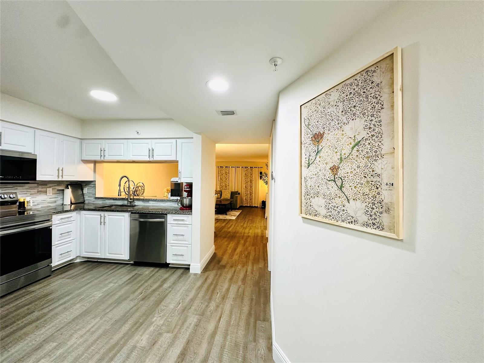 A kitchen with white cabinets and stainless steel appliances opens to a living area — 2200 S Cypress Bend Drive # 802, Pompano Beach FL 33069, POMPANO BEACH, FL