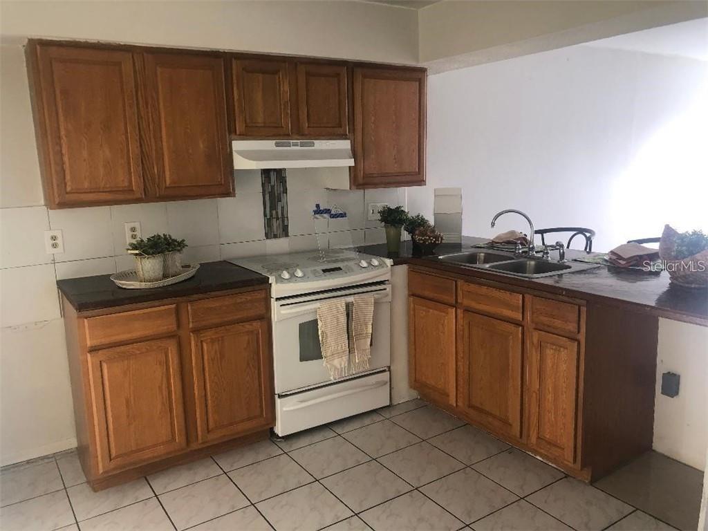 A kitchen features wood cabinets, white appliances, dark countertops, and light-colored floor tiles — 1896 CARALEE BOULEVARD UNIT 1, ORLANDO, FL