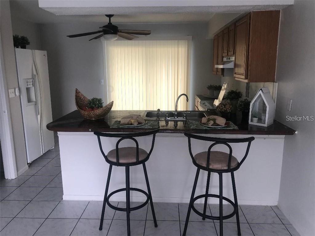 A kitchen features a breakfast bar with two stools, a sink, and wooden cabinets — 1896 CARALEE BOULEVARD UNIT 1, ORLANDO, FL