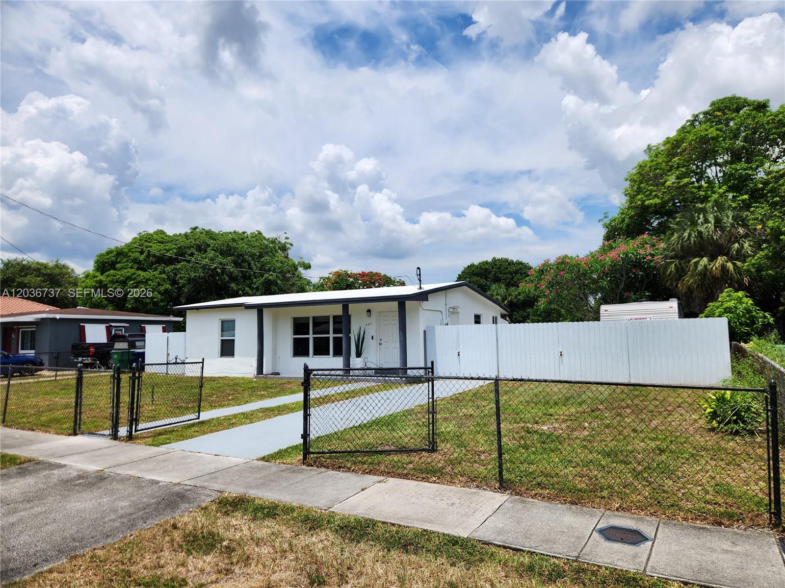 A white single-story house with a chain-link fence and a paved driveway — 721 NW 33rd Ave, Lauderhill FL 33311, LAUDERHILL, FL