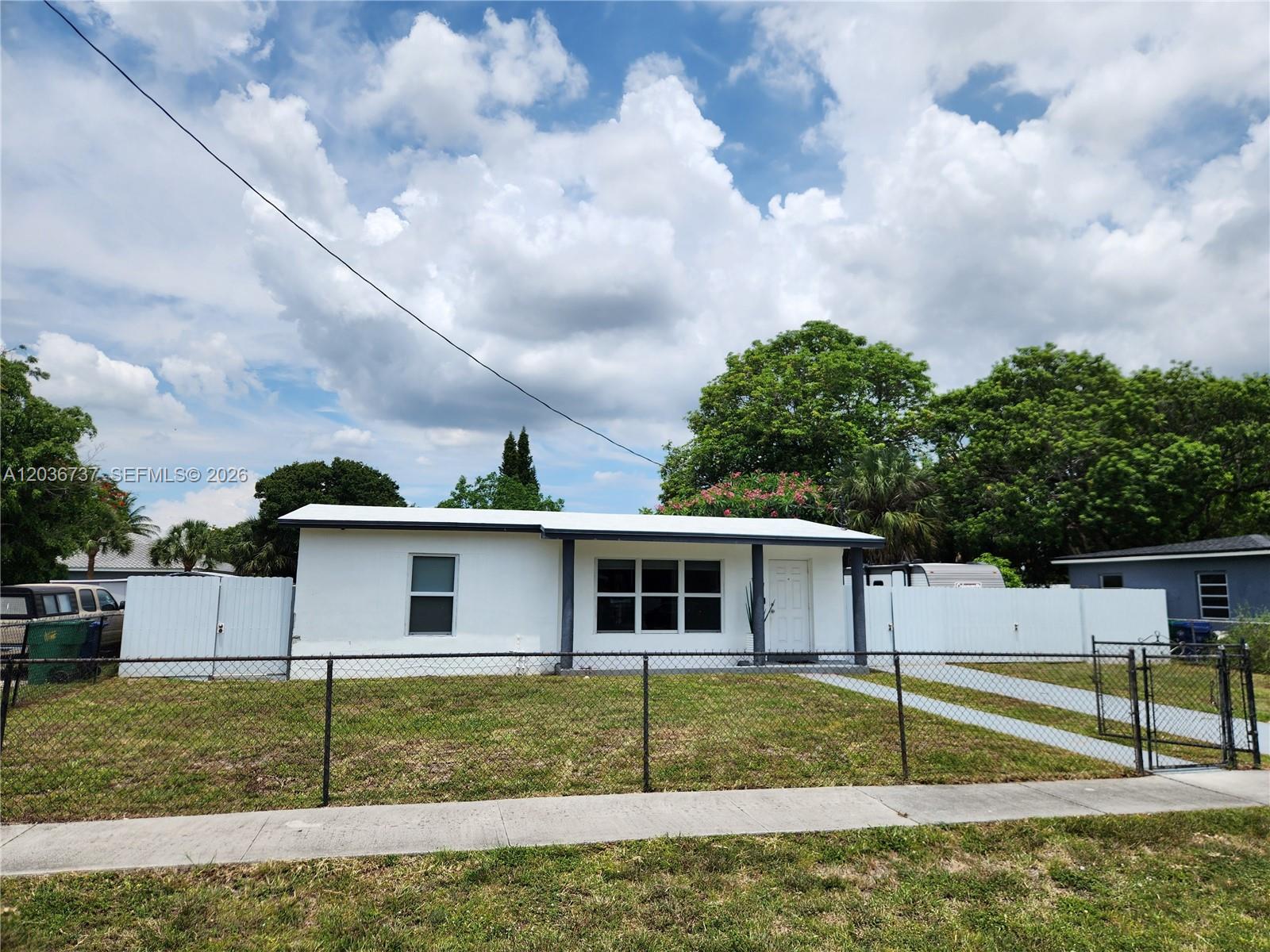 A white single-story house with a flat roof sits behind a chain-link fence — 721 NW 33rd Ave, Lauderhill FL 33311, LAUDERHILL, FL
