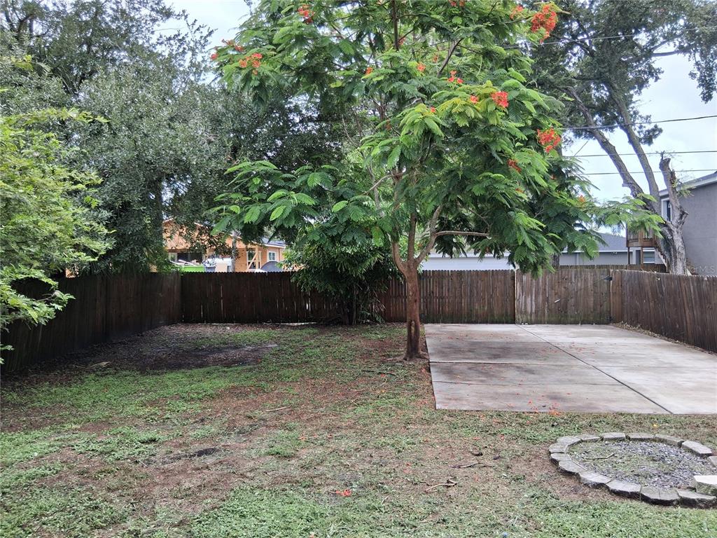 A backyard features a concrete patio, a fire pit, a flowering tree, and a wooden fence — 2736 S 3RD AVENUE S, ST PETERSBURG, FL
