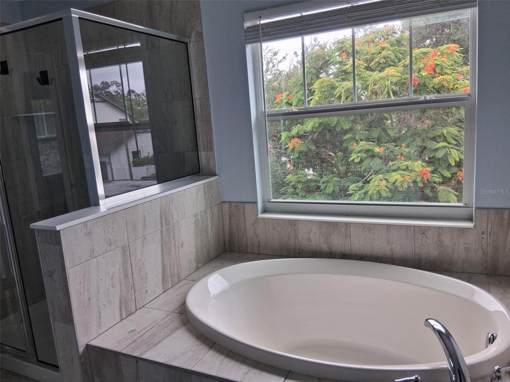 A bathroom features a tiled soaking tub, a glass-enclosed shower, and a window with foliage — 2736 S 3RD AVENUE S, ST PETERSBURG, FL