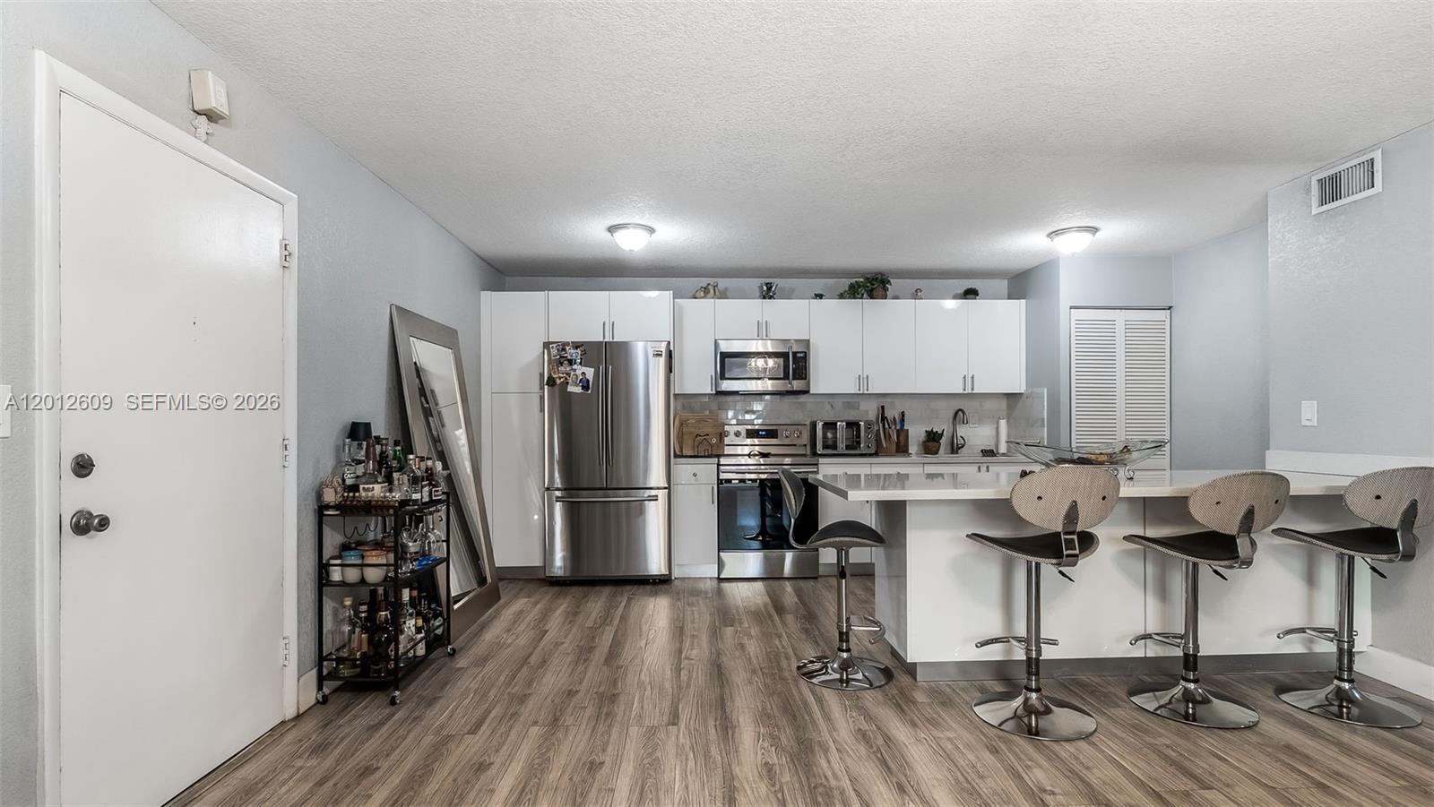 A modern kitchen features white cabinetry, stainless steel appliances, and a breakfast bar with stools — 7208 Fairway Dr # I9, Miami Lakes FL 33014, MIAMI LAKES, FL