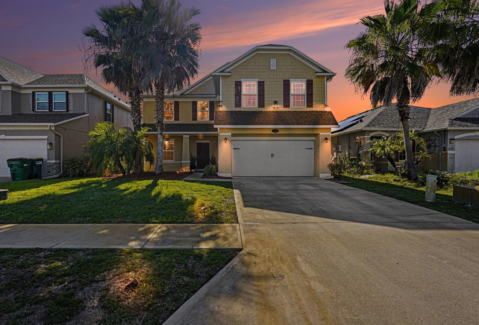 A two-story yellow house with a two-car garage and palm trees at dusk — 1688 Attilburgh Boulevard, West Melbourne FL 32904, WEST MELBOURNE, FL