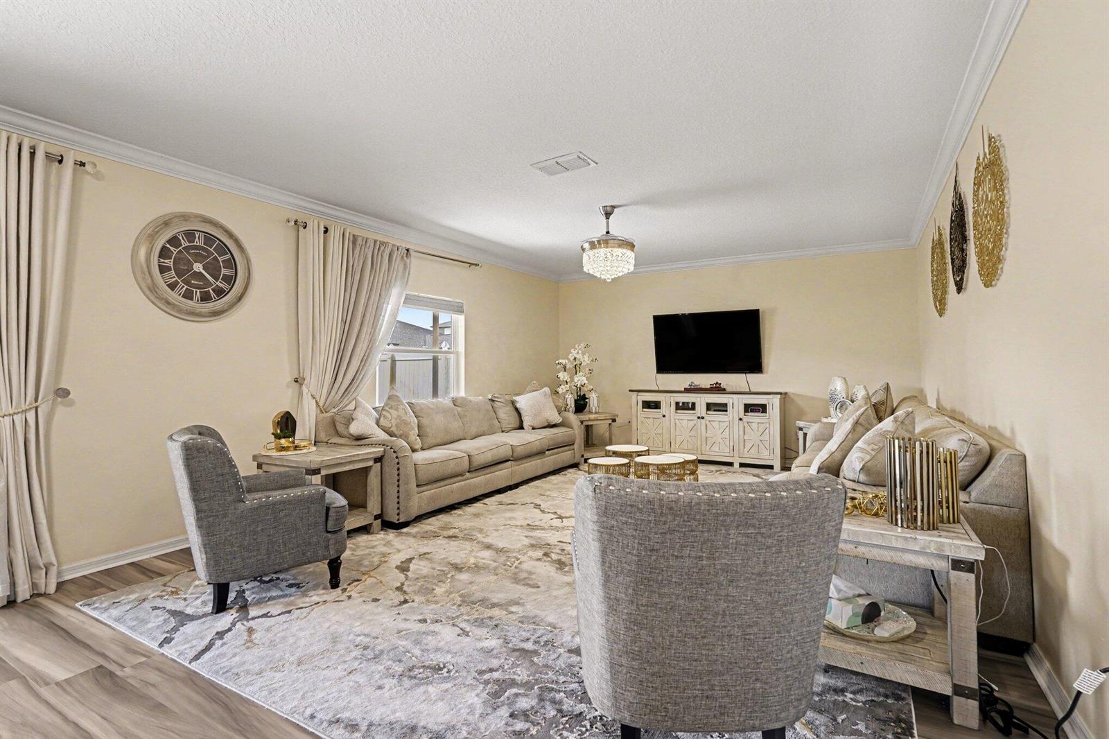 A living room features a beige sofa, two gray armchairs, a television, and area rug — 1688 Attilburgh Boulevard, West Melbourne FL 32904, WEST MELBOURNE, FL