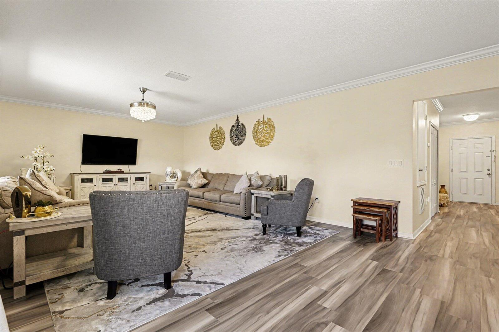 A living room features a grey sofa, two armchairs, a patterned rug, and wall decor — 1688 Attilburgh Boulevard, West Melbourne FL 32904, WEST MELBOURNE, FL