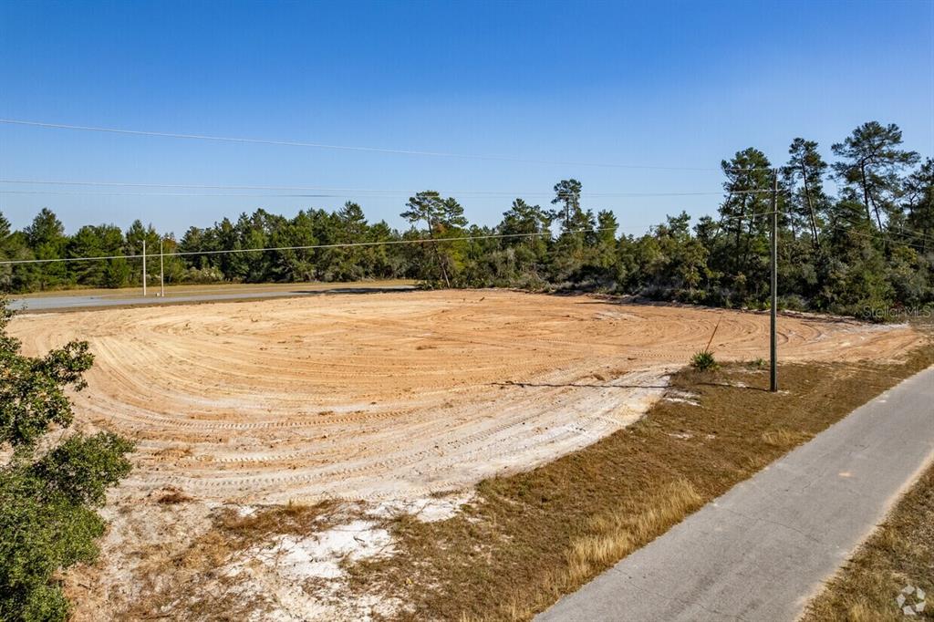An elevated view of a cleared, sandy vacant lot bordered by trees and a road — 216 SW MARION OAKS BOULEVARD SW UNIT 8, OCALA, FL