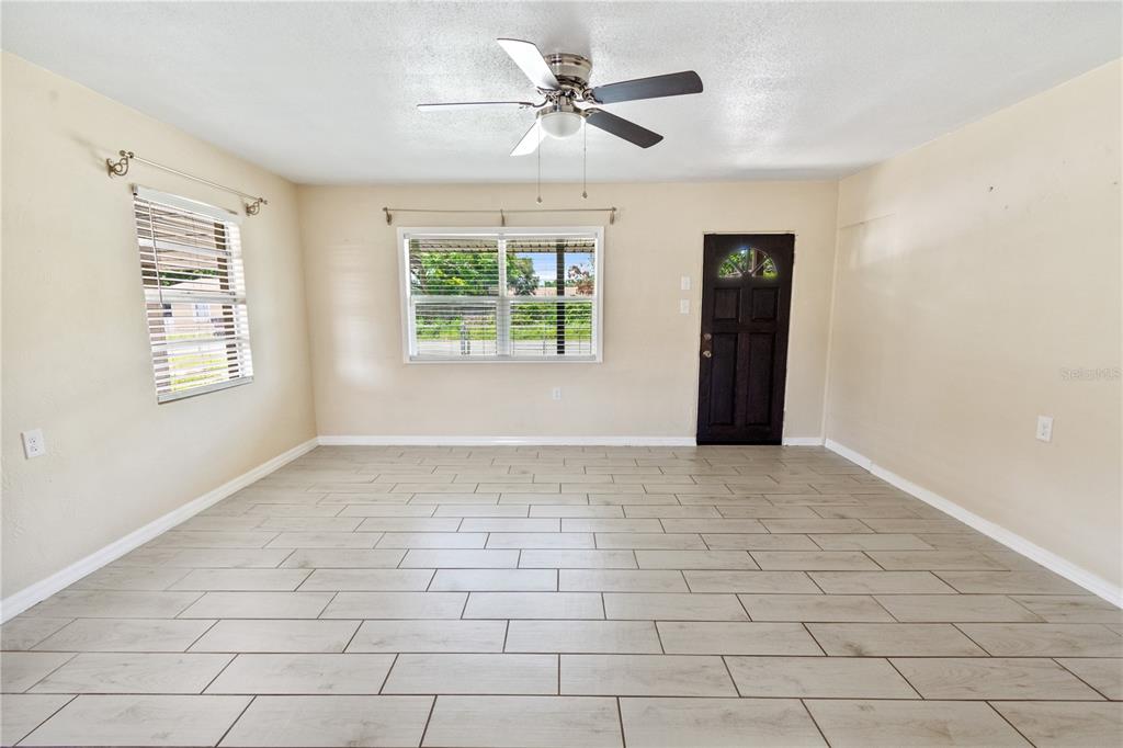 An empty living room features light-colored wood-look tile flooring, beige walls, and a ceiling fan — 404 ARMOUR AVENUE, AUBURNDALE, FL