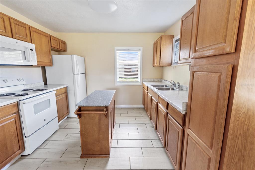 A kitchen with wood cabinets, white appliances, a small island, and light-colored tile flooring — 404 ARMOUR AVENUE, AUBURNDALE, FL