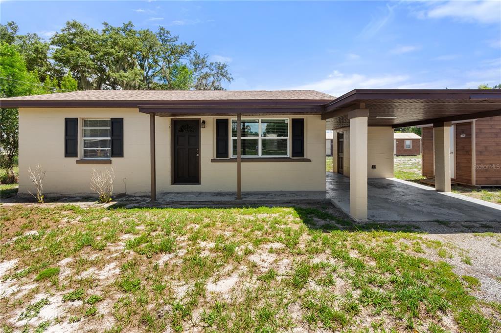 A single-story house with a tan exterior, dark shutters, and an attached carport — 404 ARMOUR AVENUE, AUBURNDALE, FL
