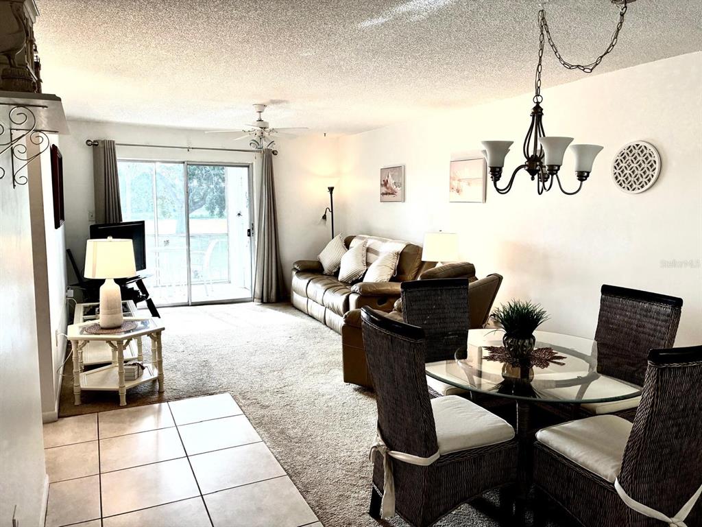 A living and dining area features beige carpet, a brown leather sofa, and glass table — 4703 1ST COURT W UNIT 393, BRADENTON, FL