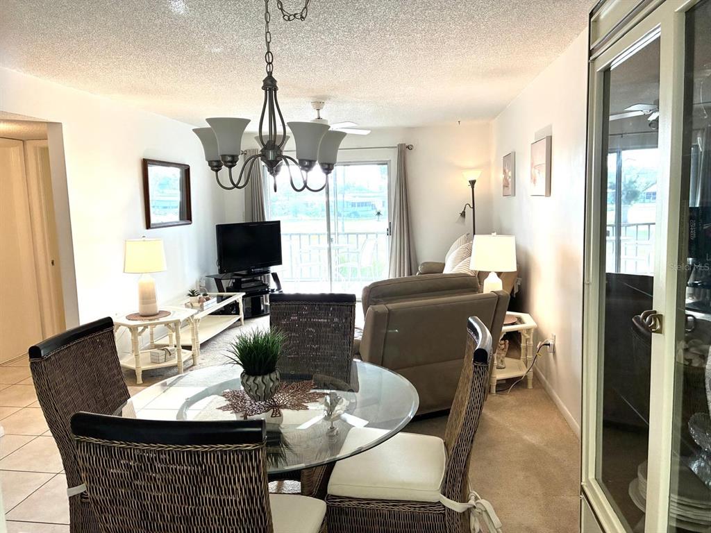 A dining area with a glass table and wicker chairs opens into a carpeted living room — 4703 1ST COURT W UNIT 393, BRADENTON, FL
