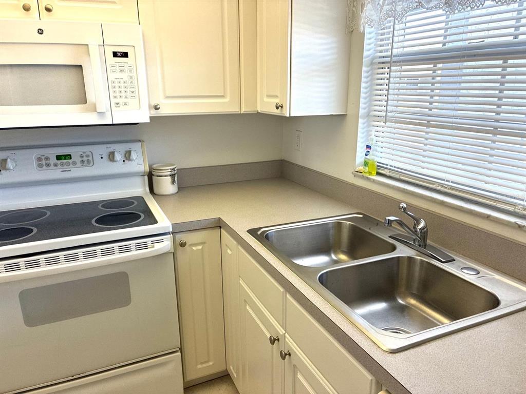 A kitchen features white cabinets, a stainless steel sink, and a white electric range — 4703 1ST COURT W UNIT 393, BRADENTON, FL