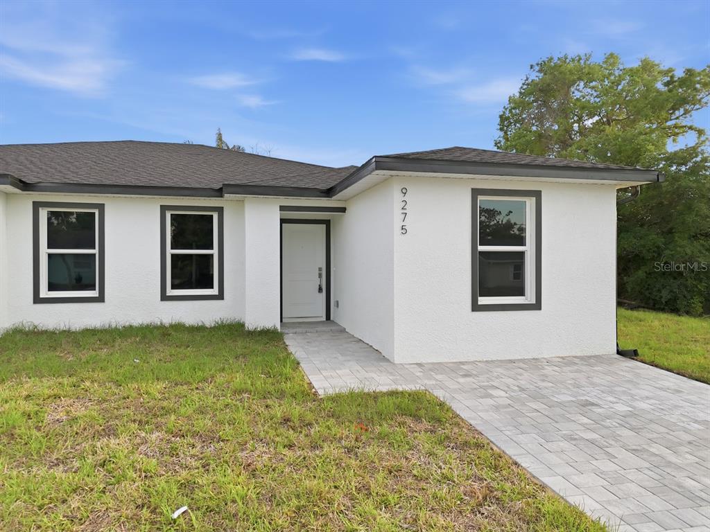 A white stucco house with a dark roof, gray trim, and a paved walkway — 9275 ANITA AVENUE, ENGLEWOOD, FL
