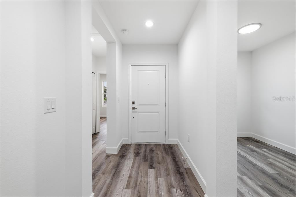 A bright entryway features white walls, a white front door, and wood-look laminate flooring — 9275 ANITA AVENUE, ENGLEWOOD, FL