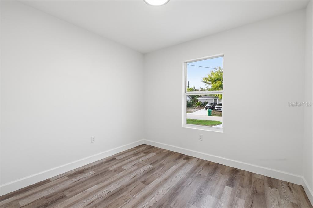 An empty room features white walls, wood-look flooring, and a single window — 9275 ANITA AVENUE, ENGLEWOOD, FL