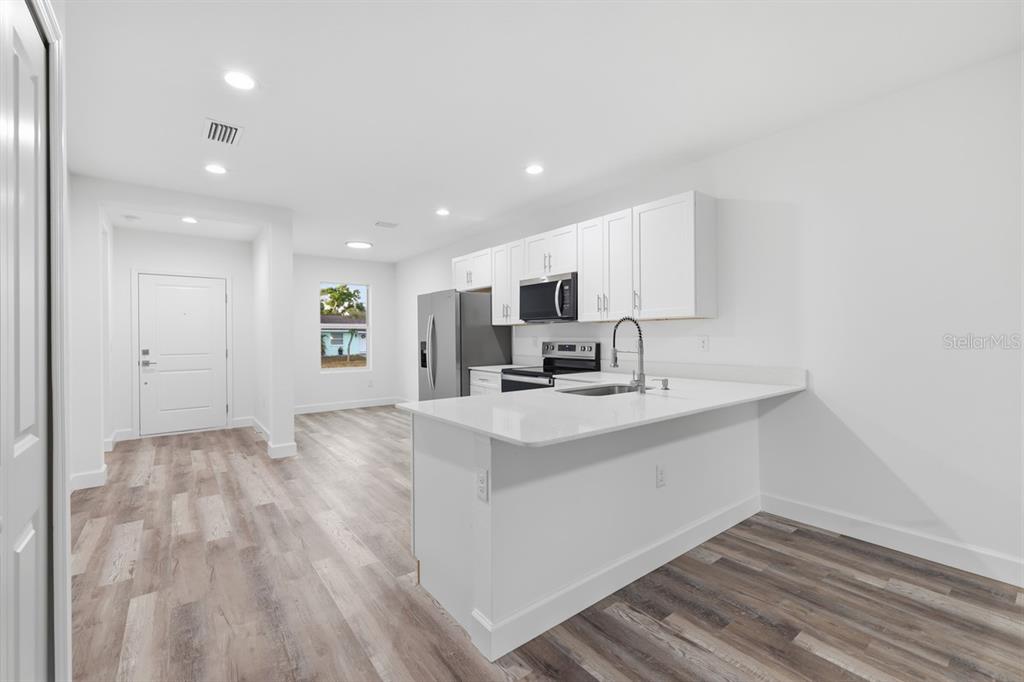 A modern kitchen features white cabinets, stainless steel appliances, and a quartz-topped peninsula island — 9275 ANITA AVENUE, ENGLEWOOD, FL