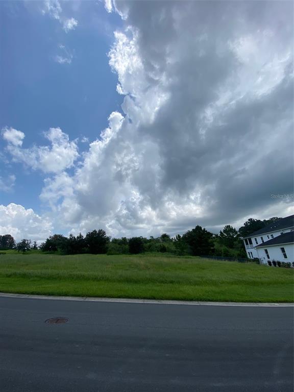 A grassy vacant lot sits next to a white house under a cloudy blue sky — 5368 GRAND SUMMIT DRIVE, BROOKSVILLE, FL