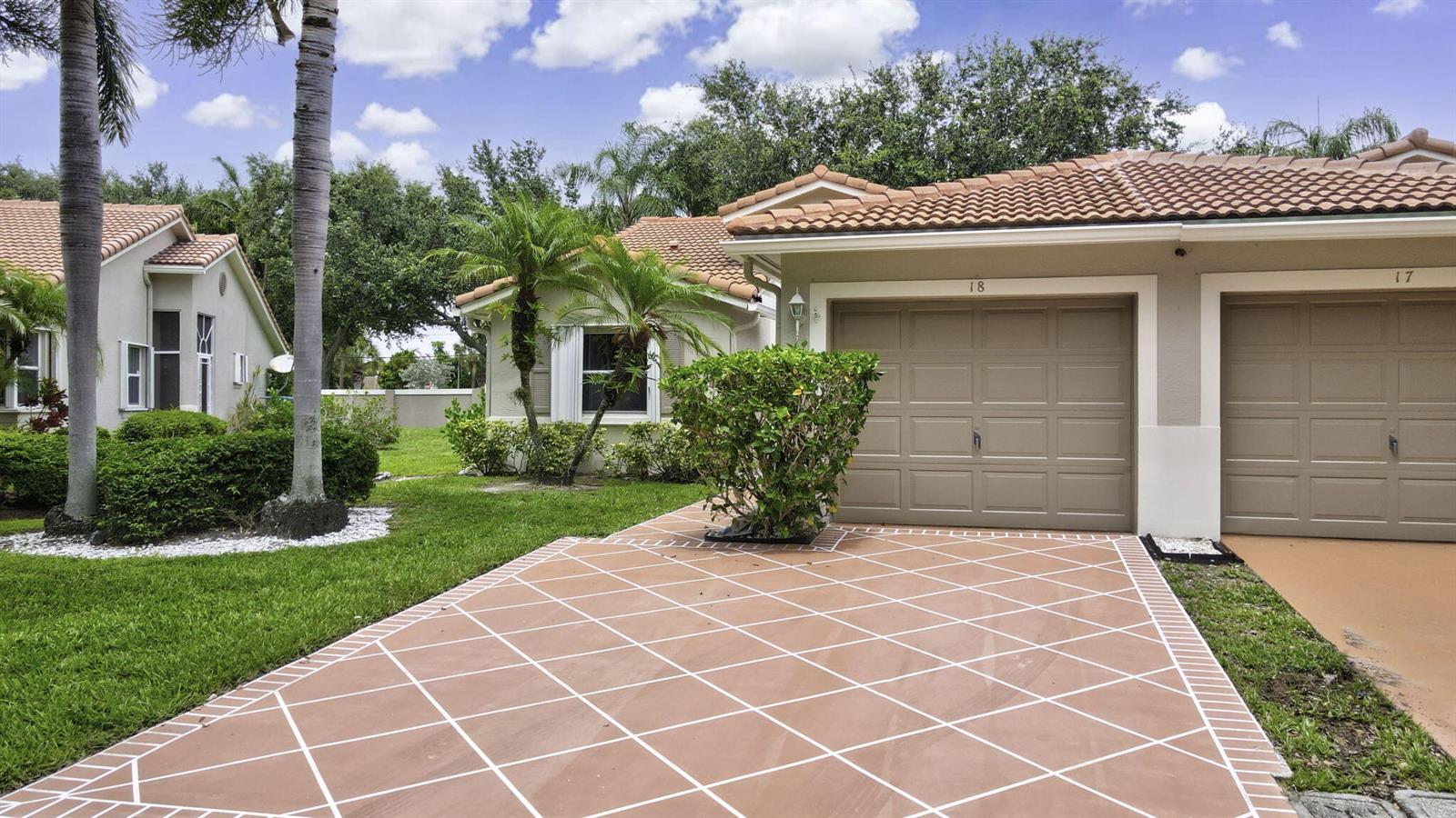 A residential exterior view shows two attached garages with a patterned driveway and landscaping — 18 Sausalito Drive, Boynton Beach FL 33436, BOYNTON BEACH, FL