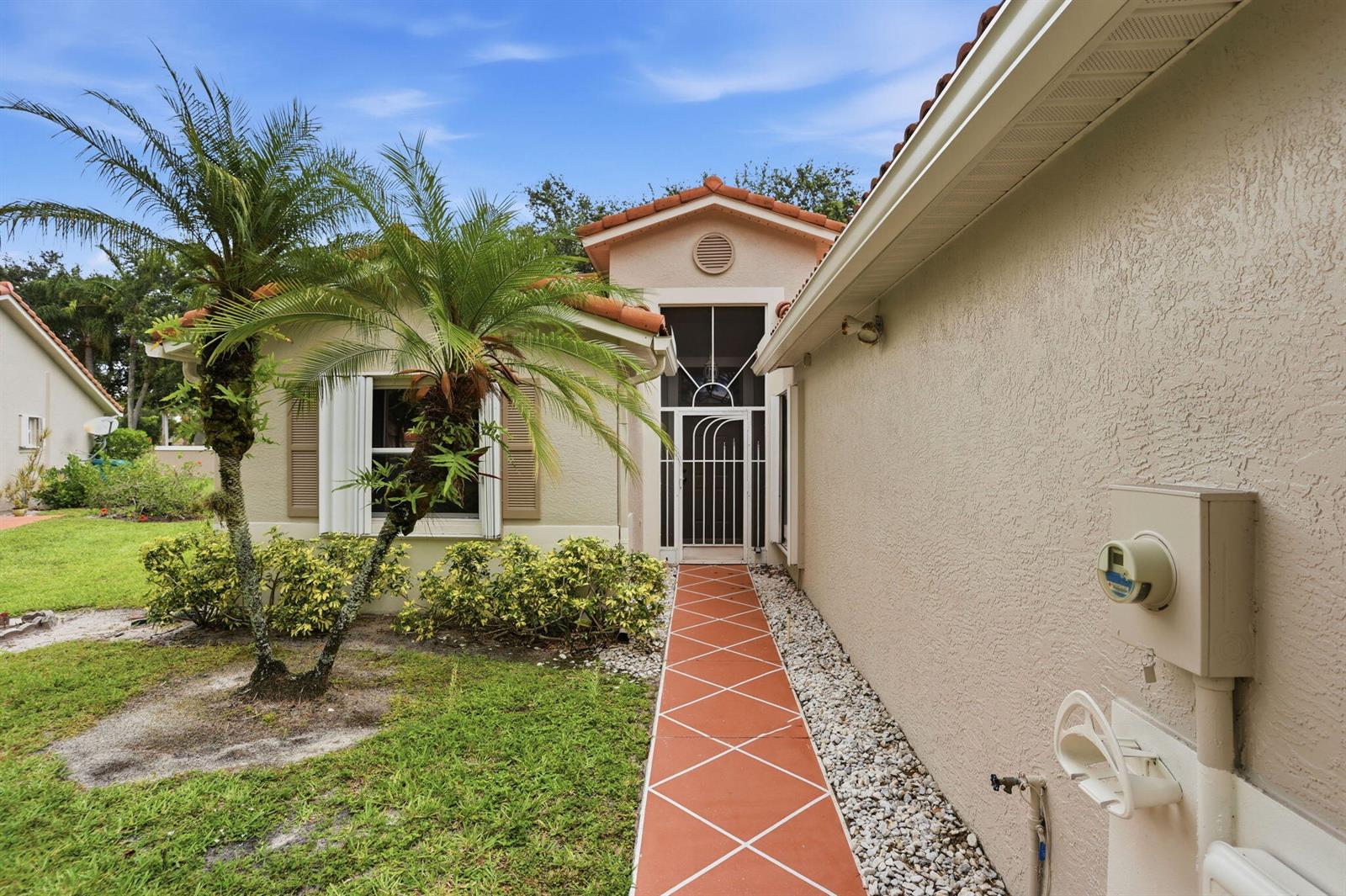 A walkway with red tiles leads to the front entrance of a beige stucco house — 18 Sausalito Drive, Boynton Beach FL 33436, BOYNTON BEACH, FL