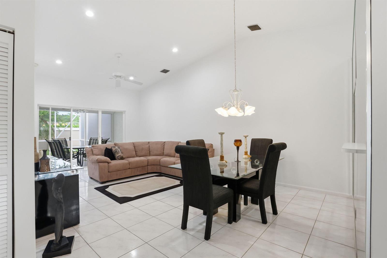 A bright open-concept living and dining area with white tile floors and a vaulted ceiling — 18 Sausalito Drive, Boynton Beach FL 33436, BOYNTON BEACH, FL