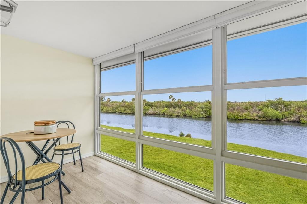 A sunroom features light wood-look flooring, a small dining set, and large windows overlooking water — VERO BEACH, FL