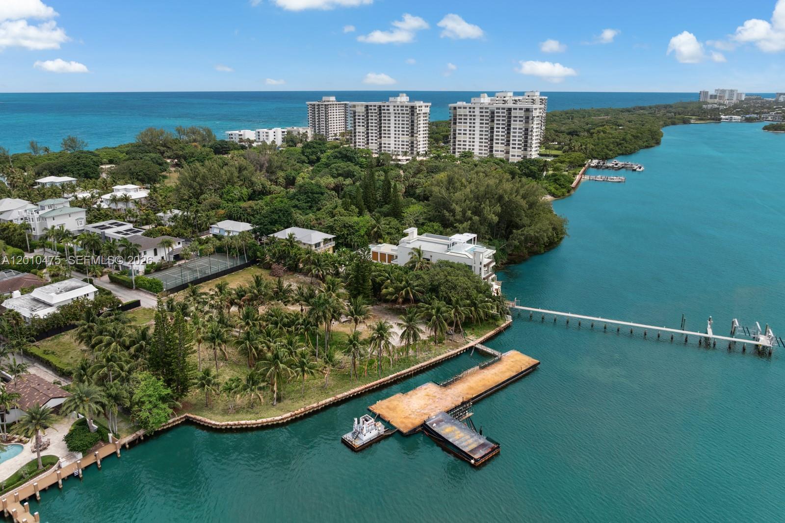 An aerial view shows a waterfront property with a large dock, tennis court, and surrounding vegetation — 910 NE 24th St, Boca Raton FL 33431, BOCA RATON, FL