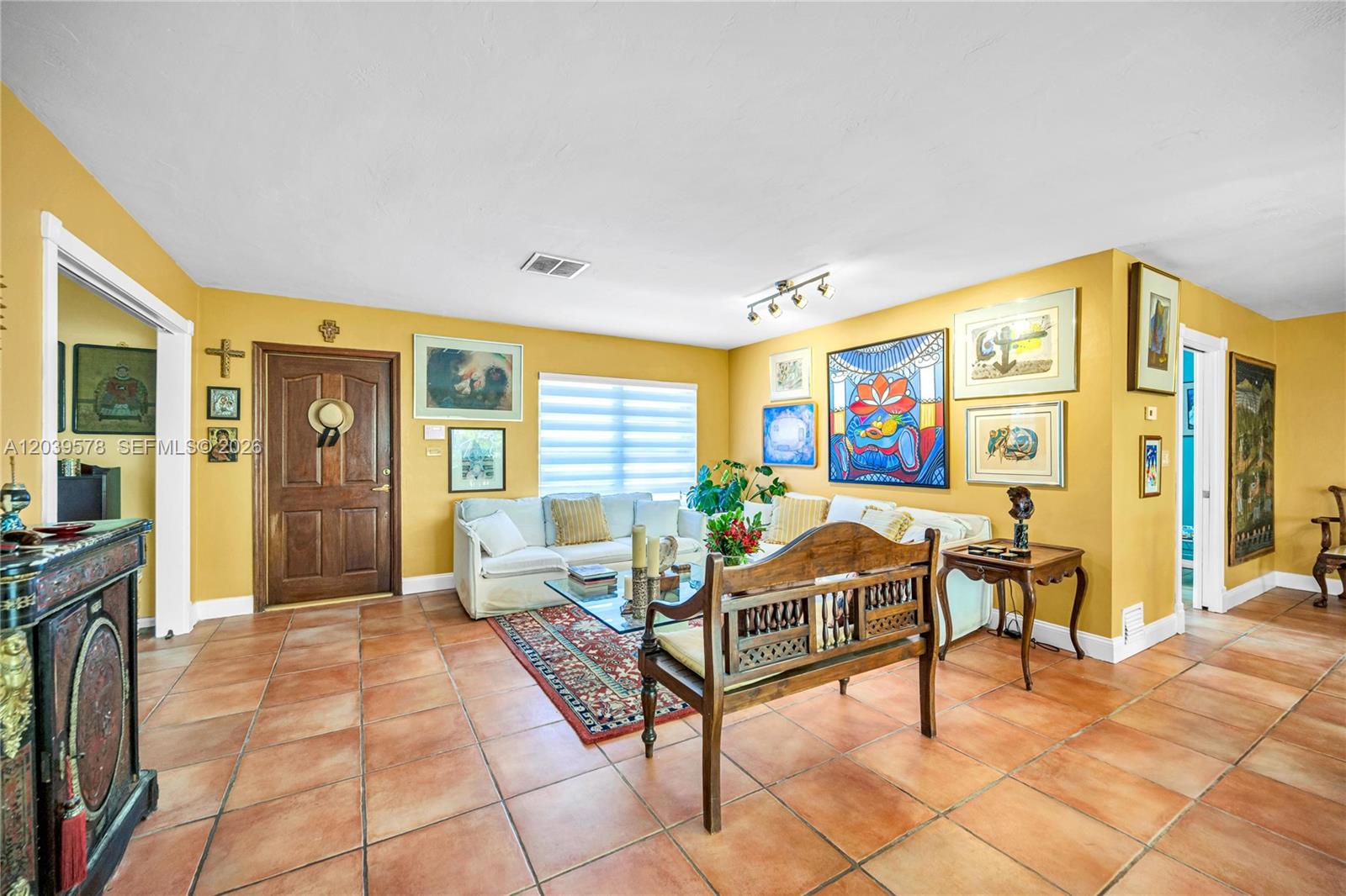 A living room features yellow walls, terracotta tile floors, a wooden bench, and eclectic artwork — 8701 SW 87th Ct, Miami FL 33173, MIAMI, FL
