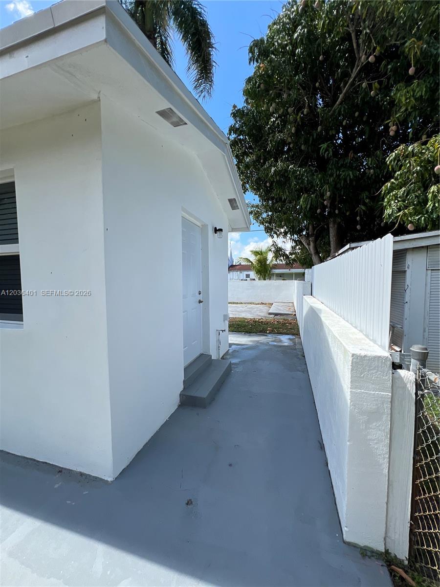 A white exterior wall features a side door and a paved walkway beside a fence — 2847 Polk St # 3, Hollywood FL 33020, HOLLYWOOD, FL