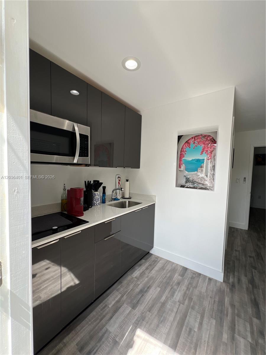 A small kitchen features glossy dark gray cabinets, white countertops, and light wood-look flooring — 2847 Polk St # 3, Hollywood FL 33020, HOLLYWOOD, FL