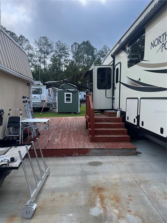 A wooden deck connects a large RV to a small shed in a paved yard — 2905 NE 104TH AVENUE UNIT 99, SILVER SPRINGS, FL