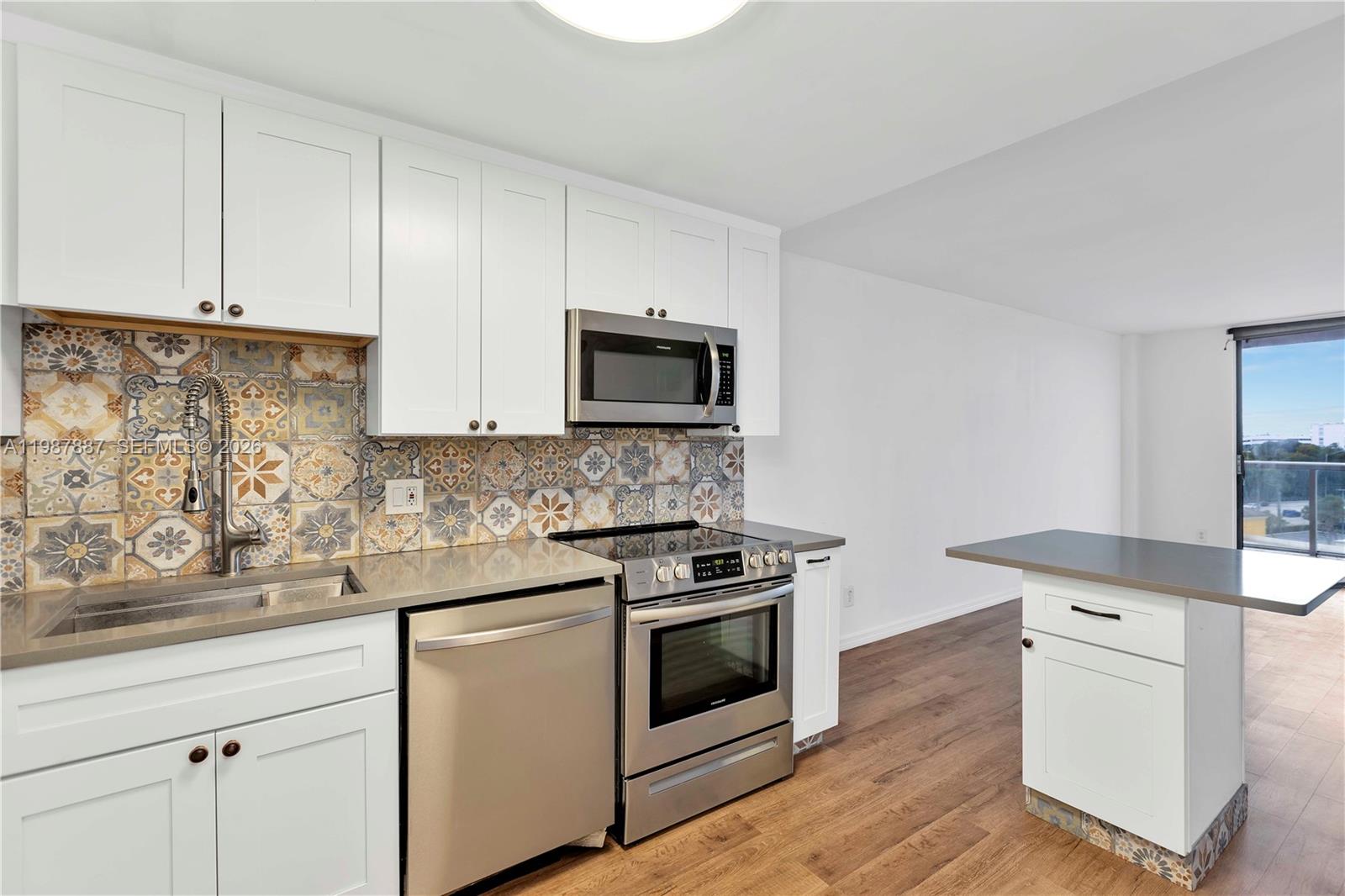 A kitchen features white cabinets, stainless steel appliances, patterned tile backsplash, and a small island — 13499 Biscayne Blvd # 613, North Miami FL 33181, NORTH MIAMI, FL