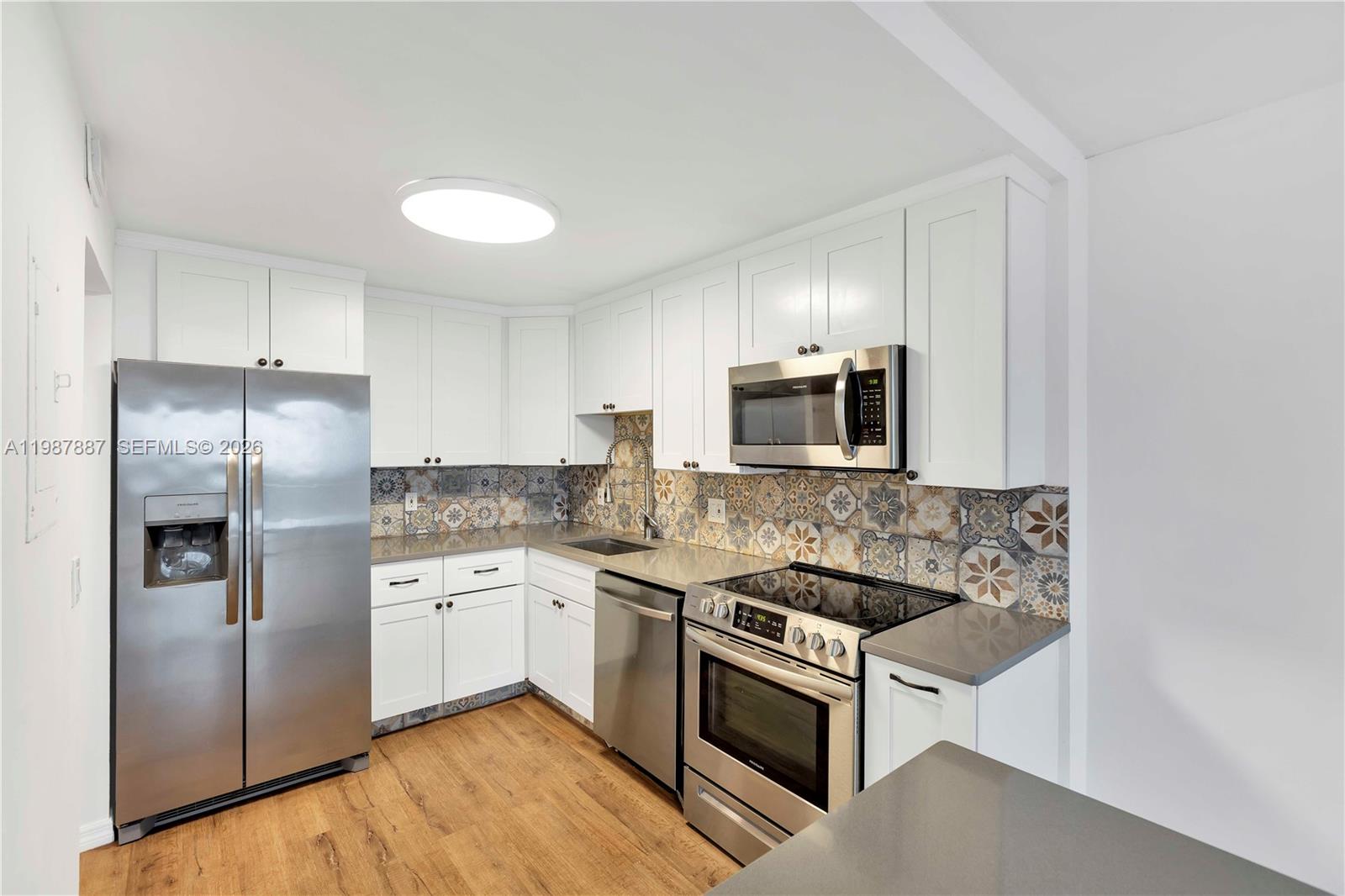 A kitchen features white cabinets, stainless steel appliances, gray countertops, and patterned tile backsplashes — 13499 Biscayne Blvd # 613, North Miami FL 33181, NORTH MIAMI, FL