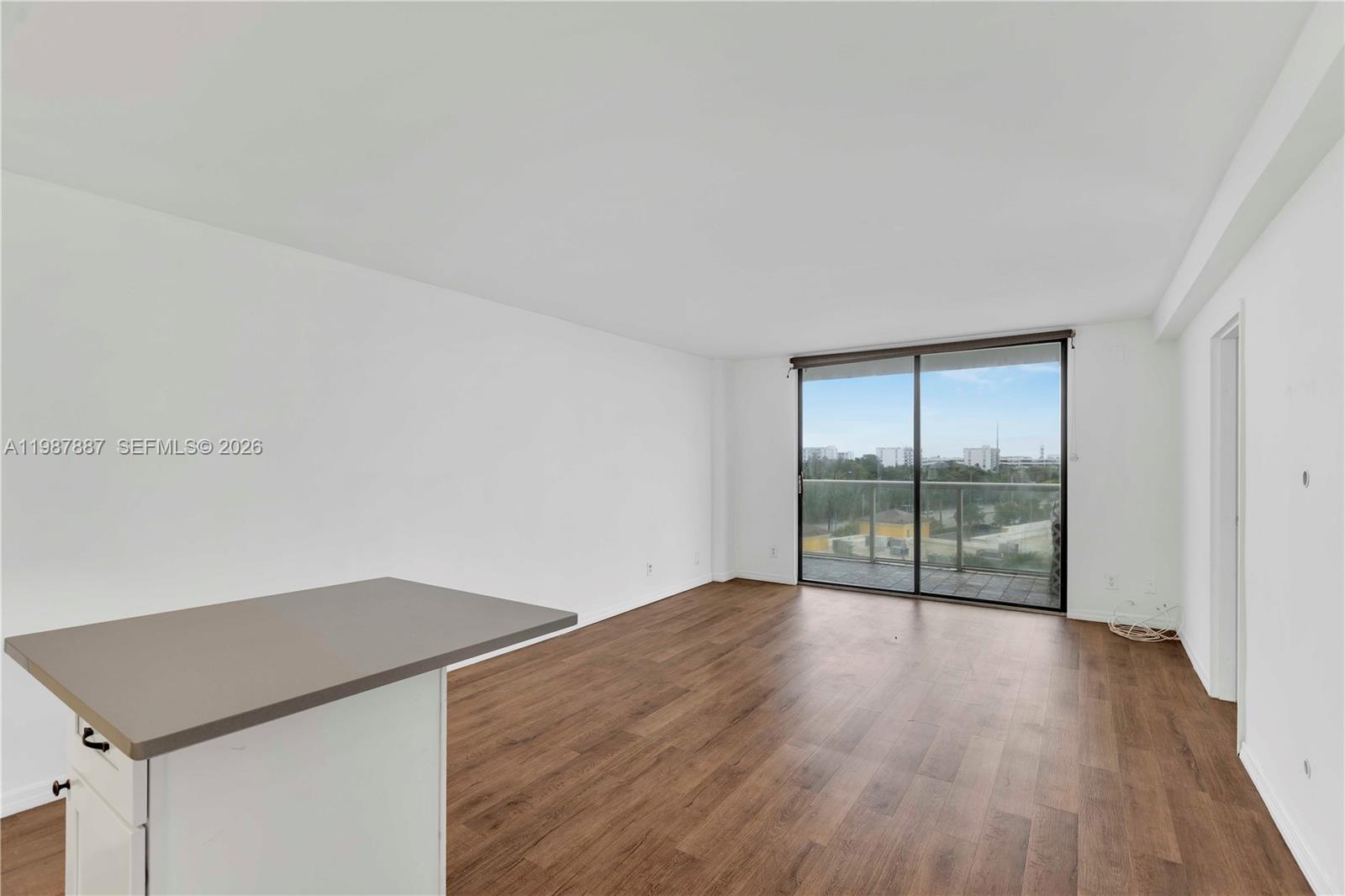 An empty room with wood-look flooring, a kitchen island, and a sliding glass balcony door — 13499 Biscayne Blvd # 613, North Miami FL 33181, NORTH MIAMI, FL