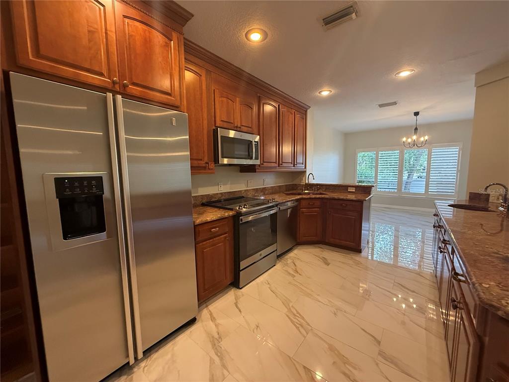 A kitchen with wood cabinets, stainless steel appliances, granite countertops, and light-colored tile flooring — 1195 SHIPWATCH CIRCLE, TAMPA, FL