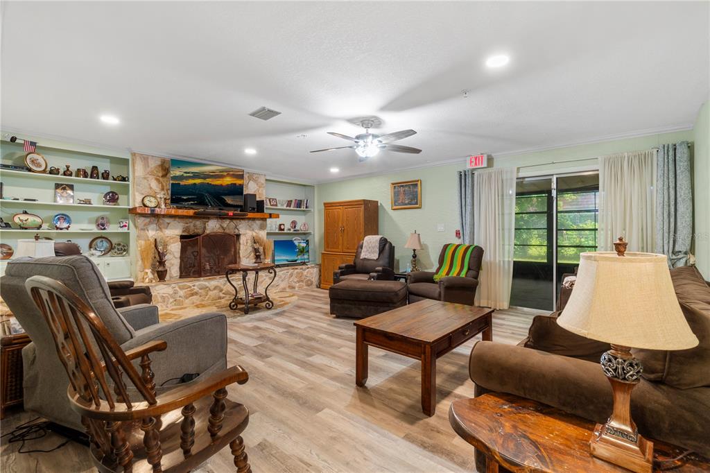 A living room features a stone fireplace, built-in shelving, wood-look flooring, and sliding glass doors — 207 W WHEELER ROAD, SEFFNER, FL