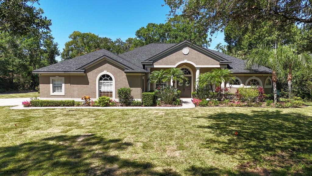 A single-story house with a brown stucco exterior, dark shingled roof, and landscaped front yard — 5852 CACHETTE DE RIVIERA COURT, NEW PORT RICHEY, FL