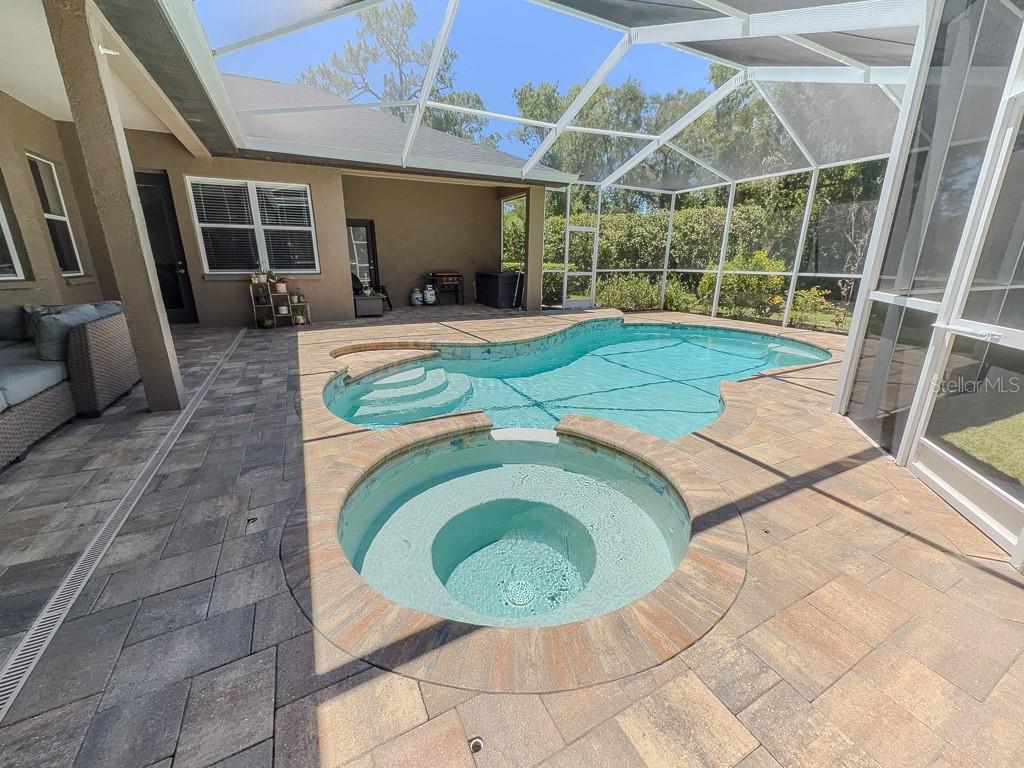 A screened-in patio features a swimming pool, a circular spa, and paver decking — 5852 CACHETTE DE RIVIERA COURT, NEW PORT RICHEY, FL